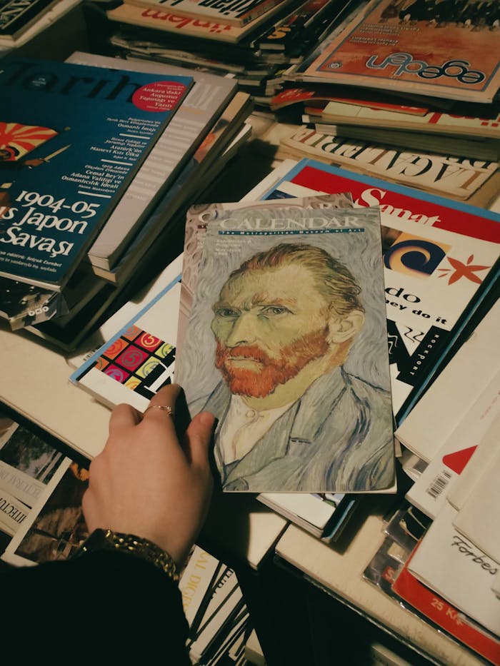 A hand holds a Vincent van Gogh calendar among various publications in a bookstore.